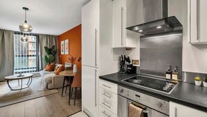 A modern kitchen with white cabinets, a stainless steel range hood, and a black countertop. - Modern 1BR • 2 min to Tube • O2 & ExCeL (London)