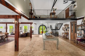 A spacious loft with a high ceiling, a staircase, a dining area, and a library.