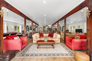 A spacious living room with a pool table, red sofas, a wooden coffee table, and a large mirror reflecting the room.