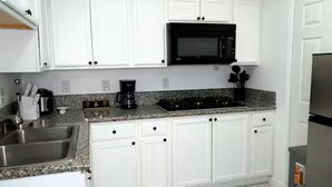 A kitchen with white cabinets, a black microwave, a stainless steel sink, and a granite countertop.