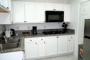 Una cocina con armarios blancos, un microondas negro, un lavamanos de acero inoxidable y una encimera de granito.