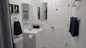 A bathroom with a toilet, sink, and mirror. There are towels hanging on the wall and a door.