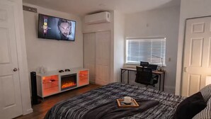 A bedroom with a bed, a TV, a fireplace, a desk, and a window.