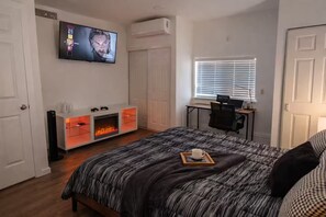 A bedroom with a bed, a TV, a fireplace, a desk, and a window.