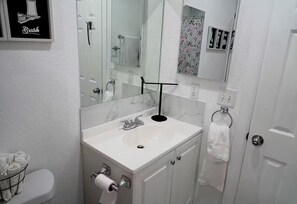 Une salle de bain avec un lavabo blanc, un miroir, des toilettes et une douche.