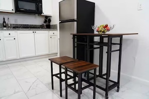 Une cuisine avec des meubles blancs, un réfrigérateur noir, une table en bois et un chariot en métal.
