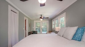 A bedroom with a large bed, a ceiling fan, and a view through a door.