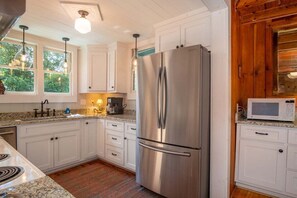 Una cocina con armarios blancos, un refrigerador de acero inoxidable, un microondas y luces colgantes.