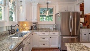 A kitchen with white cabinets, a stainless steel refrigerator, a granite countertop, and pendant lighting.