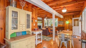 A wooden cabin interior with a dining area, kitchen, and a large cabinet with glass doors.