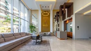 A spacious lobby with a large sofa, a coffee table, and a rug. There is a reception desk with a modern design and a sign that reads "Brickell Apartments."