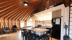 A spacious loft-style kitchen with a high ceiling, wooden beams, a central island with chairs, and a built-in oven. - The Black Bear Yurt: Rustic Hilltop Escape with Stunning Bear Lake Views – Sleeps 12! (Garden City)