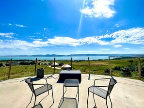 En terrasse med udendørs siddepladser, udsigt til et sø og fjerne bjerge.