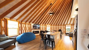A spacious living area with a high ceiling, wooden beams, a large bean bag, a kitchen area with a bar, and a television. - The Black Bear Yurt: Rustic Hilltop Escape with Stunning Bear Lake Views – Sleeps 12! (Garden City)