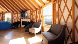 Una habitación acogedora con vigas de madera, un ventanal grande, un televisor de pantalla plana y asientos cómodos.