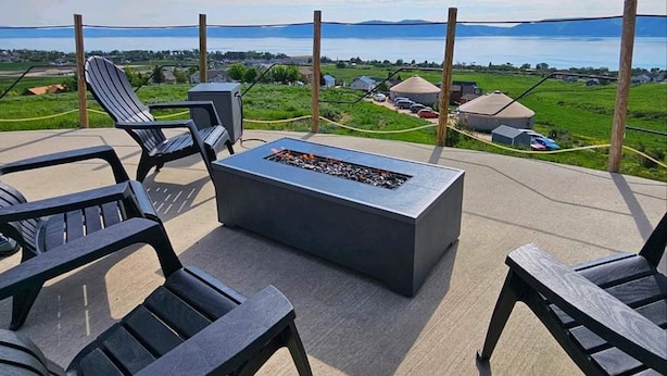 Un patio al aire libre con un pozo de fuego y sillones de descanso, con vista a un paisaje pintoresco con montañas y una masa de agua.