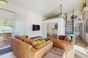 Een moderne woonkamer met een bank, een salontafel en een televisie. Er is een trap die naar een andere kamer leidt.