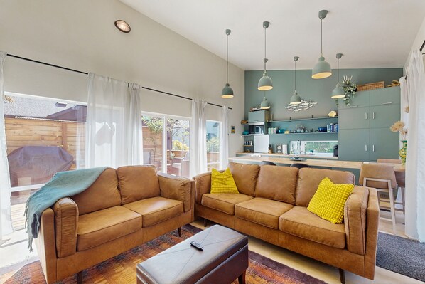 Een moderne woonkamer met twee bruine leren banken, een salontafel en een keuken met groene kasten en hanglampen.
