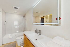 Een moderne badkamer met een grote spiegel, een wit wastafelmeubel en een bad.