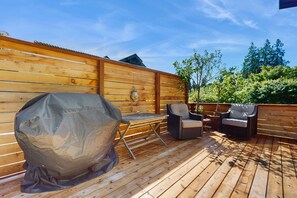 Een houten terras met een barbecue, twee stoelen en een tafel.