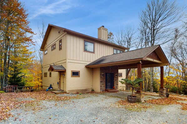A two-story house with a covered porch, a stone fireplace, and a gravel driveway.
