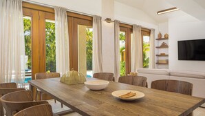 A modern dining area with a wooden table, chairs, and a bowl of food. - Roga Villa- Wellness, Tropical, Pool, Sauna, Ice Bath, 5 min to Encuentro beach (Encuentro Ocean Caberete)