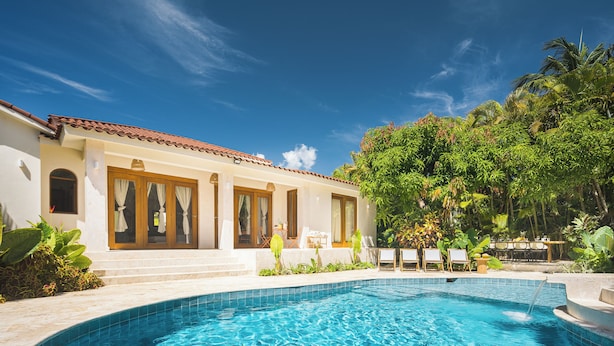 A swimming pool with clear blue water, a white building with a tiled roof, and lush greenery surrounding the area. - Roga Villa- Wellness, Tropical, Pool, Sauna, Ice Bath, 5 min to Encuentro beach (Encuentro Ocean Caberete)