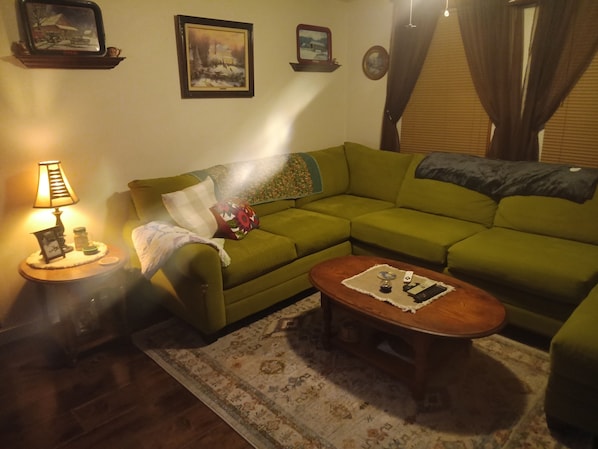 A living room with a green sofa, a wooden coffee table, a patterned rug, a lamp on a side table, and wall-mounted pictures.