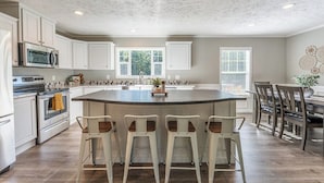 A kitchen with white cabinets, a central island with bar stools, a microwave, and a stove. - Spacious Lodge w/ Fire Pit & Hot Tub (Wallingford)