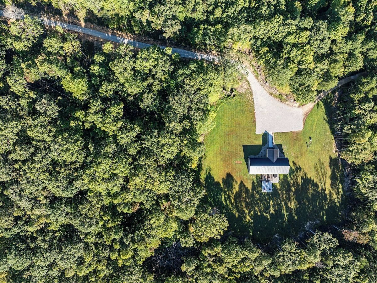An aerial view of a building surrounded by dense forest, with a clear path leading to the entrance.