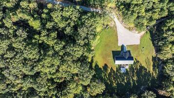 An aerial view of a building surrounded by dense forest, with a clear path leading to the entrance.