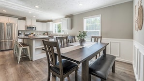 A modern kitchen with white cabinetry, a central island, and a dining area with wooden chairs and a bench. - Spacious Lodge w/ Fire Pit & Hot Tub (Wallingford)