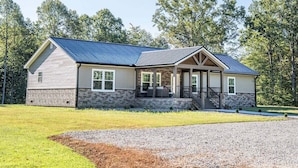 A two-story house with a stone foundation, a blue roof, and a front porch. - Spacious Lodge w/ Fire Pit & Hot Tub (Wallingford)