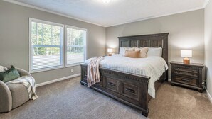 A bedroom with a large bed, two bedside tables, a chair, and a window. - Spacious Lodge w/ Fire Pit & Hot Tub (Wallingford)