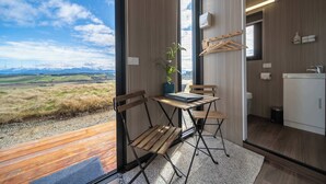 A modern room with a wooden table and chairs, a small plant, and a view of the countryside. - Whitestone Retreat 1 by Tiny Away (Hillside)