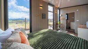A modern hotel room with a large bed, a view of mountains, and a kitchenette. - Whitestone Retreat 1 by Tiny Away (Hillside)