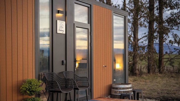 A modern building with a wooden exterior, a glass door, and a bench outside. - Whitestone Retreat 1 by Tiny Away (Hillside)