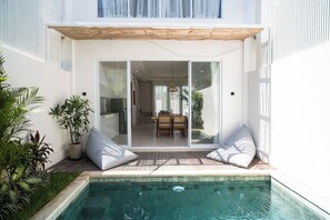 Ett modernt hus med en swimmingpool, skjutdörrar i glas som leder till en matplats och en pergola över uteplatsen.