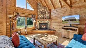 A cozy cabin interior with a stone fireplace, wooden walls, a television, and a comfortable seating area. - Mountain Escape on 6 acres w Hot Tub & Privacy (Baker)