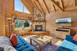 A cozy cabin interior with a stone fireplace, wooden walls, a television, and a comfortable seating area.