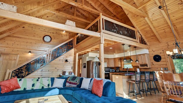 A wooden cabin interior with a blue sofa, kitchen area, and a staircase leading to an upper level. - Mountain Escape on 6 acres w Hot Tub & Privacy (Baker)