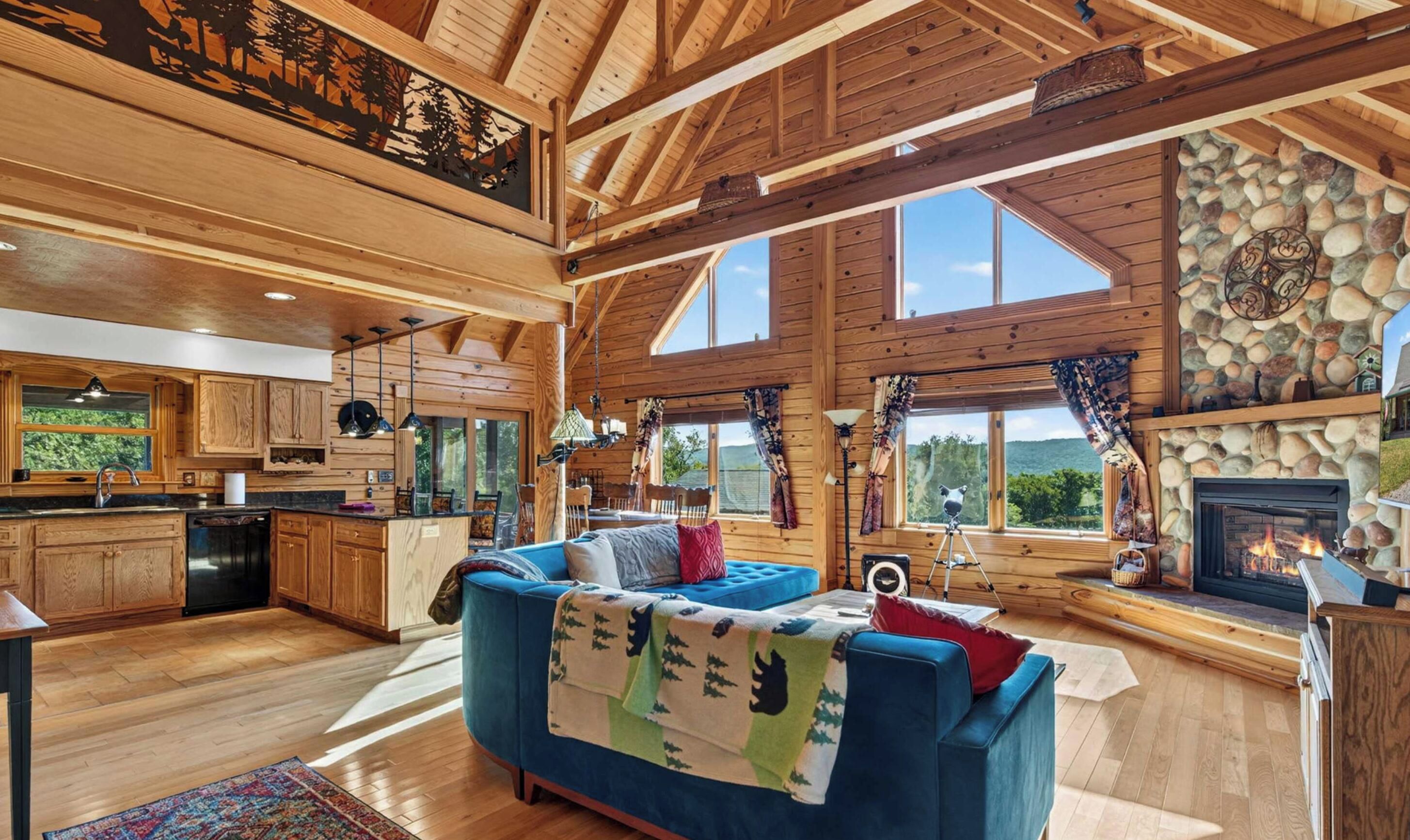 A spacious living area with a fireplace, wooden beams, and a large window overlooking a scenic landscape.