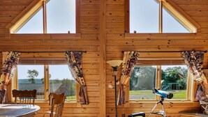 A cabin with a high ceiling, wooden walls, and large windows. There is a table with chairs, a lamp, and a telescope. - Mountain Escape on 6 acres w Hot Tub & Privacy (Baker)