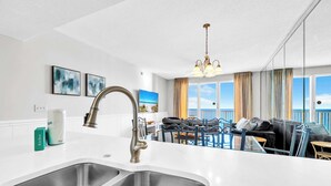A modern kitchen with a double sink, a chandelier, and a view of the ocean through large windows. - Majestic Sun 805A | Unobstructed Views, 8th Floor! | Close to Shops & Dining | Perfect Weekend Getaway Spot! (Miramar Beach)