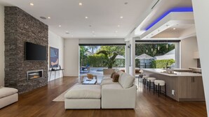 A modern living room with a stone fireplace, a large flat-screen TV, and a cozy seating area. - West Hollywood Haven: Pool, Chef’s Kitchen & More (Los Angeles)