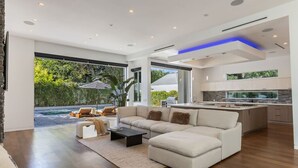 A modern living room with a sectional sofa, a coffee table, and a view of a swimming pool and outdoor seating area. - West Hollywood Haven: Pool, Chef’s Kitchen & More (Los Angeles)