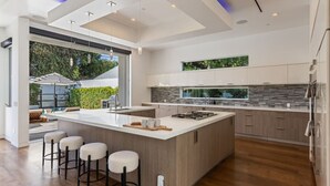 A modern kitchen with a large island, bar stools, and a view of the outdoors. - West Hollywood Haven: Pool, Chef’s Kitchen & More (Los Angeles)