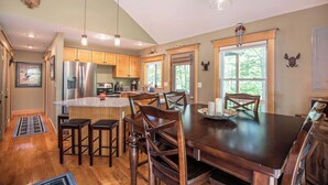 A spacious kitchen with wooden cabinets, a large island, and a dining area with a dark wooden table and chairs. - Finley Lodge | 5 Mins to Attitash | Game Room (Bartlett)