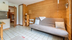 A cozy room with a sofa, a small table, a cabinet, and a wooden wall. - Champel A : Appartement lumineux, panorama alpin (LE GRAND BORNAND)