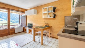 A compact kitchen with a dining area, wooden walls, and a view of the outdoors. - Champel A : Appartement lumineux, panorama alpin (LE GRAND BORNAND)